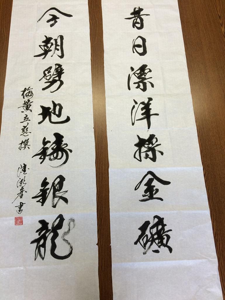 Black Chinese calligraphy couplet on two vertical cloth strips with red seal stamp.