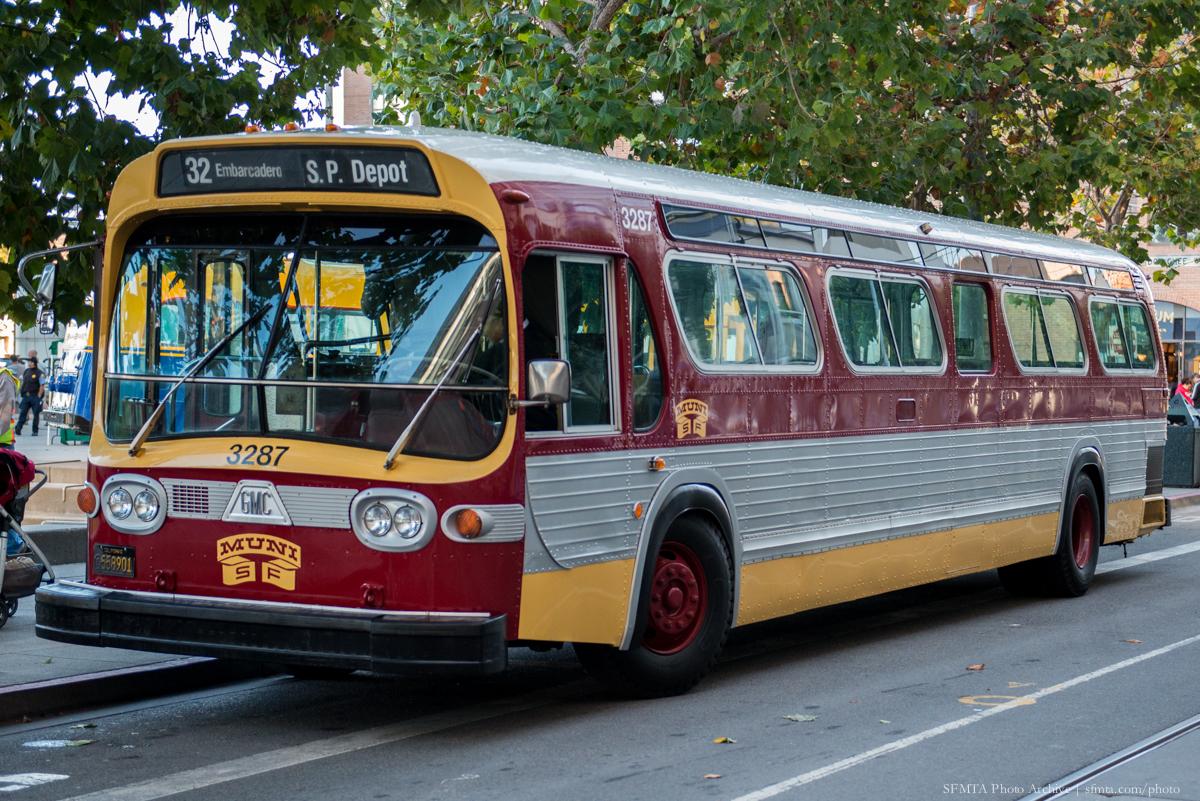 Gold and maroon vintage Muni bus number 3287 parked on city street with trees overhead.