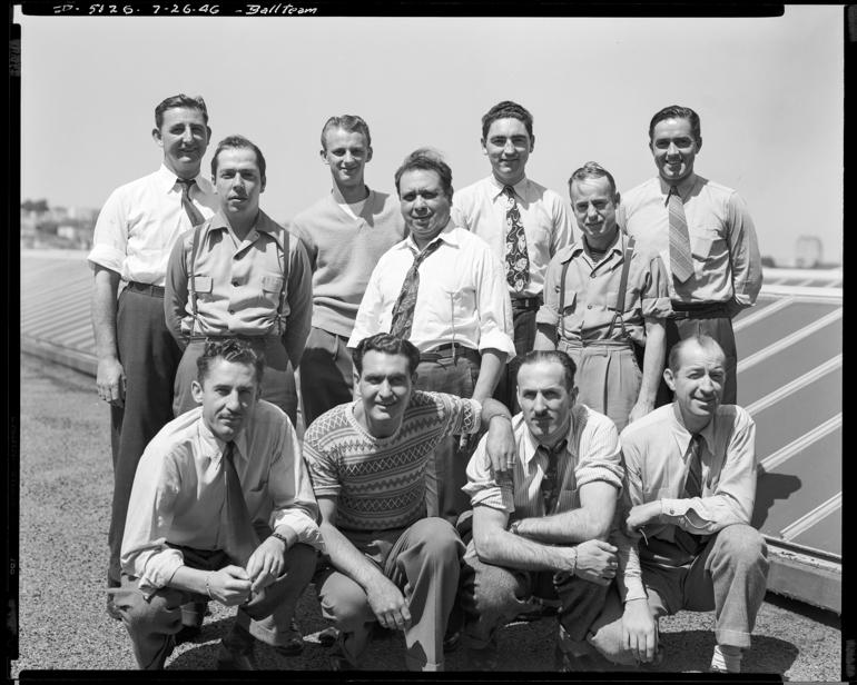 Eleven men posing on a rooftop, four kneeling in front and seven standing behind, July 26, 1946.
