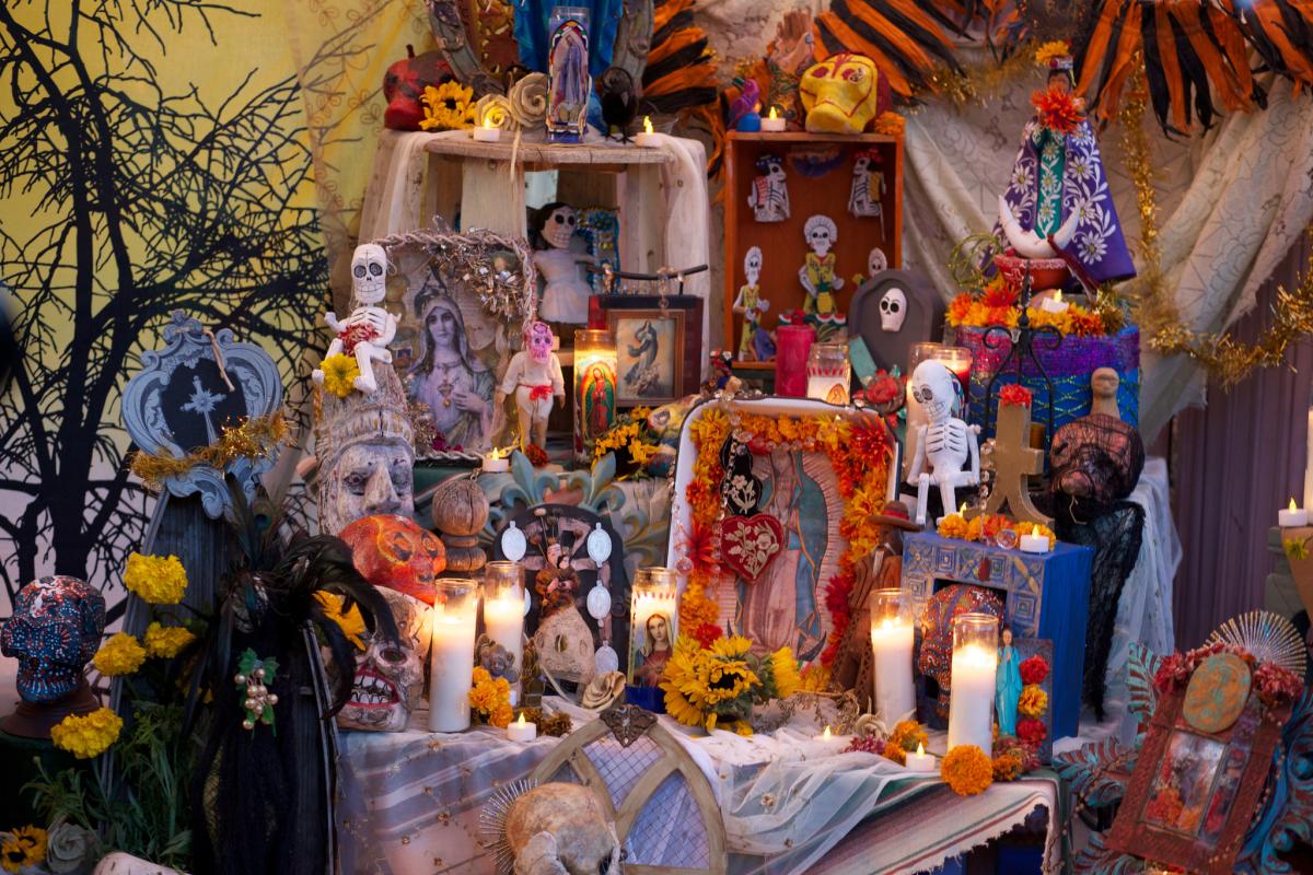 Colorful Day of the Dead altar with marigolds, candles, skulls, religious images, and decorative elements.