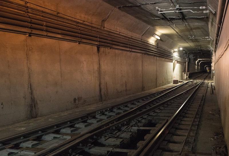 Muni Metro subway tunnel with dual tracks and overhead lighting extending into the distance.