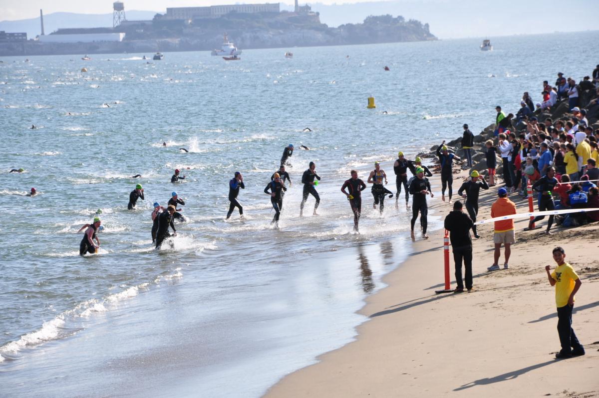 Swimmers exit the water during the Escape From Alcatraz Triathlon with Alcatraz Island visible in the background.