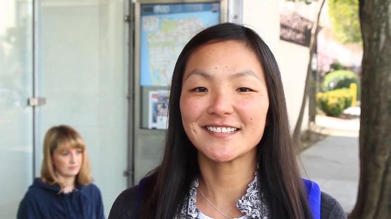 Woman smiling at camera in transit station with passenger visible in background