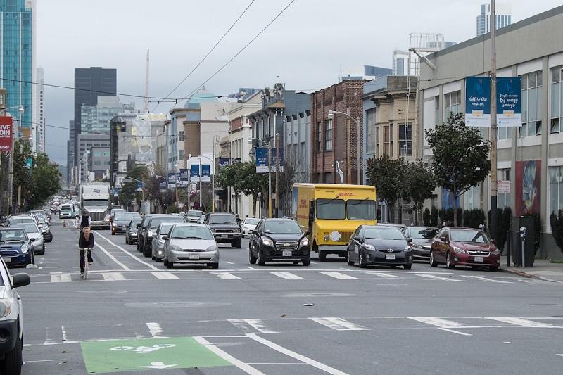 Folsom Street intersection with parked and moving vehicles, yellow taxi, bike lane, and urban buildings.