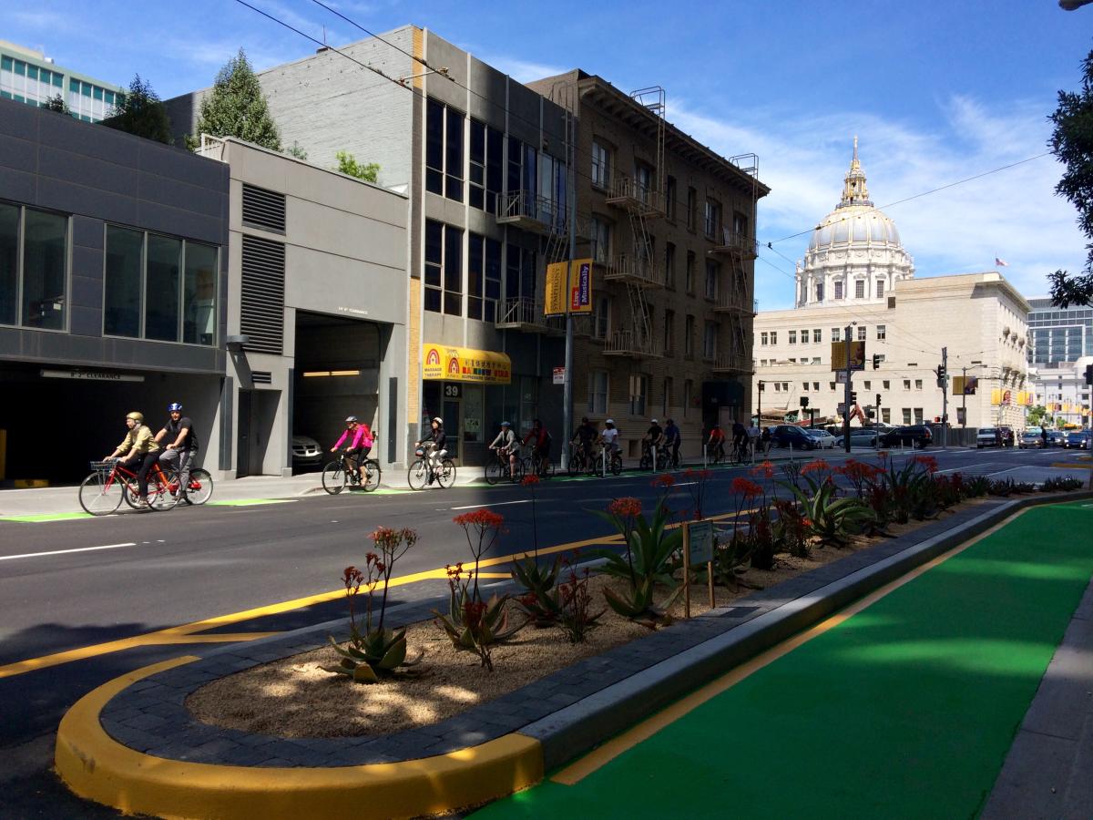 Cyclists ride on Polk Street contraflow bike lane with City Hall dome visible in background.