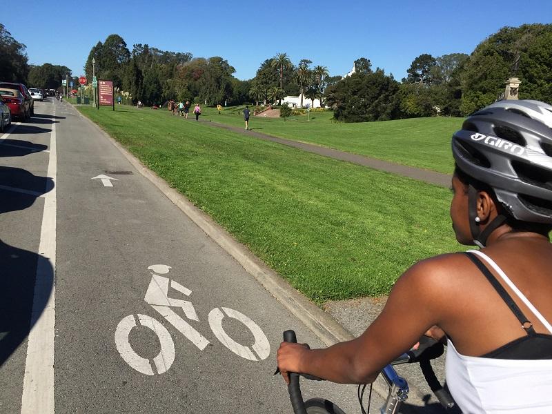 Cyclist riding on bike lane in Golden Gate Park with grassy field and trees visible ahead