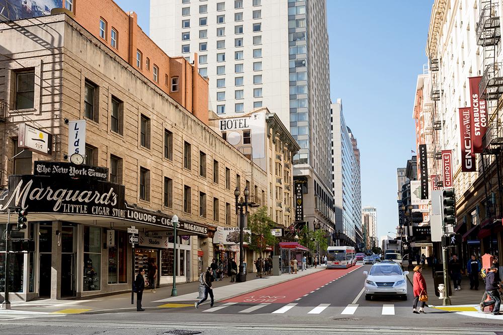 Downtown street intersection with red transit lane, pedestrians, and historic storefronts