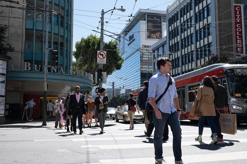 Pedestrians and a red Muni bus on a busy Market Street intersection in downtown San Francisco.