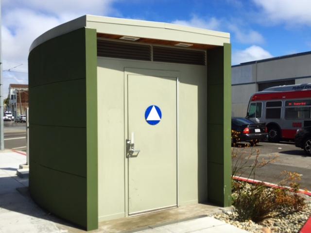 Green and beige rectangular convenience station with blue transit logo on cream-colored doors.
