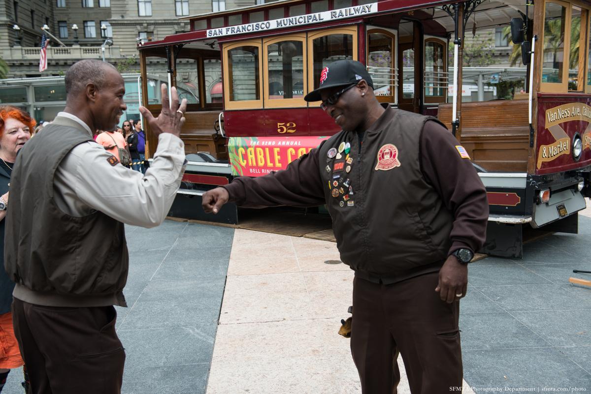 Two men greet each other in front of a San Francisco cable car numbered 52 at Union Square.
