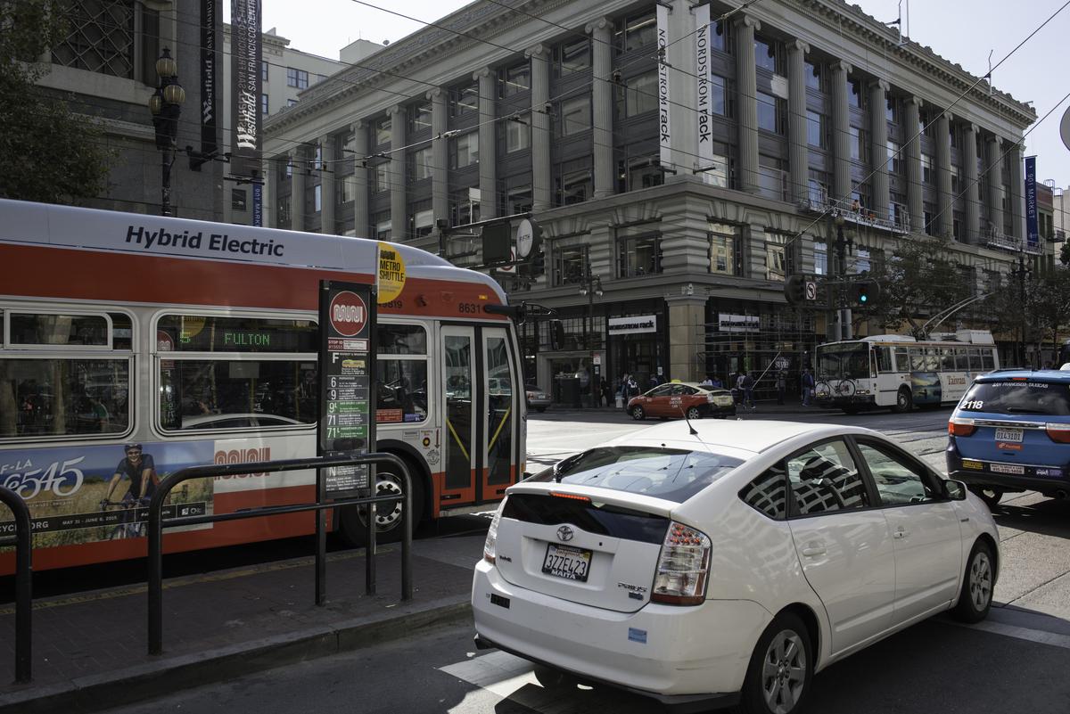 Hybrid Electric bus traveling west on Market Street at 5th Street with cars and taxis in downtown traffic.
