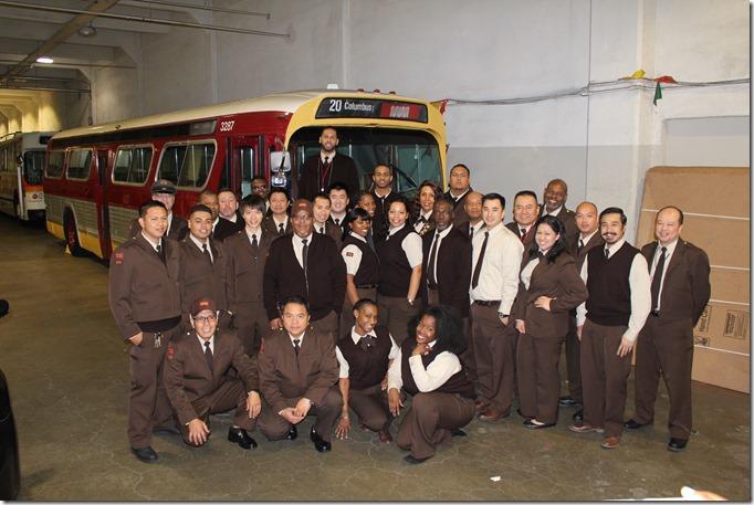 Muni bus operator graduates pose in front of a vintage coach at Presidio Division facility.