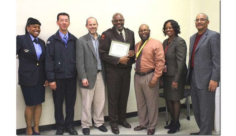 Seven transit agency staff members stand together, with a man in the center holding a certificate.