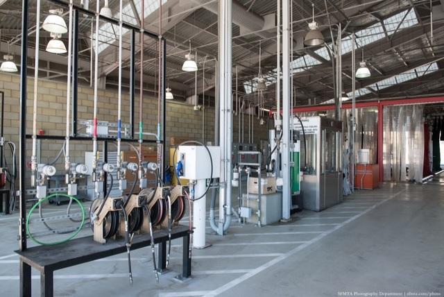 Interior of transit bus maintenance facility with service bays, equipment, and overhead lighting.
