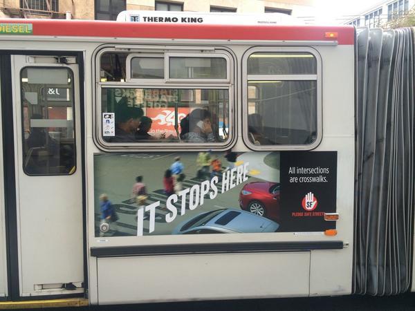 Red and white transit bus with "It Stops Here" safety campaign advertisement on side, passengers visible through windows.