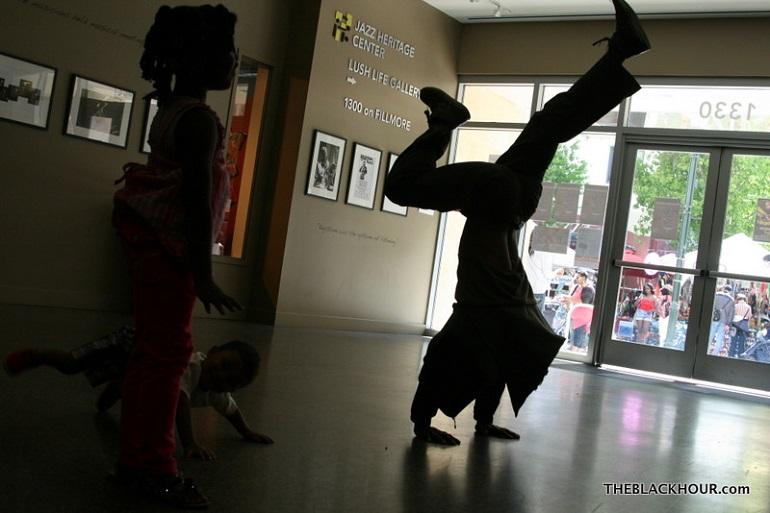 Silhouette of dancer performing handstand in lobby while children watch through glass doors.