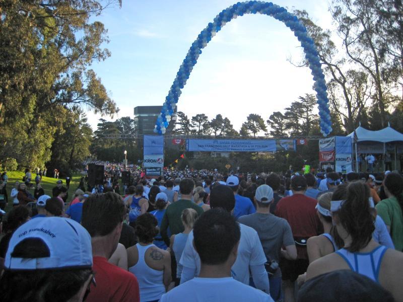 Large crowd gathered at blue arch finish line in Golden Gate Park during KP Half Marathon event.