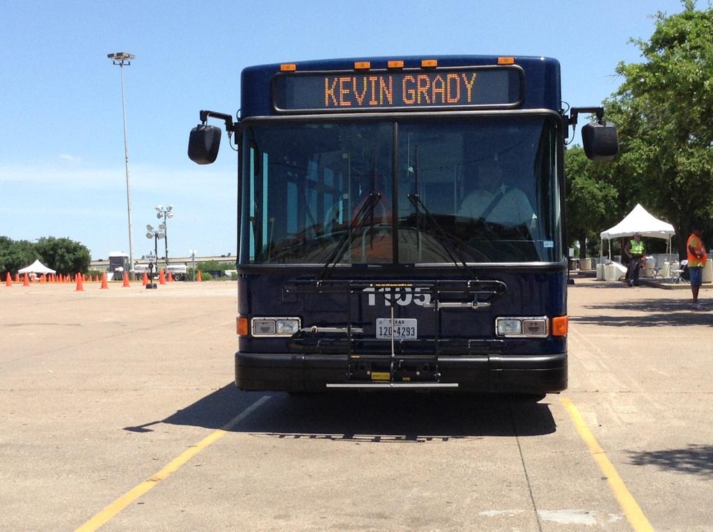 Dark blue transit bus with "Kevin Grady" displayed on head sign, parked in empty lot during bus roadeo competition.