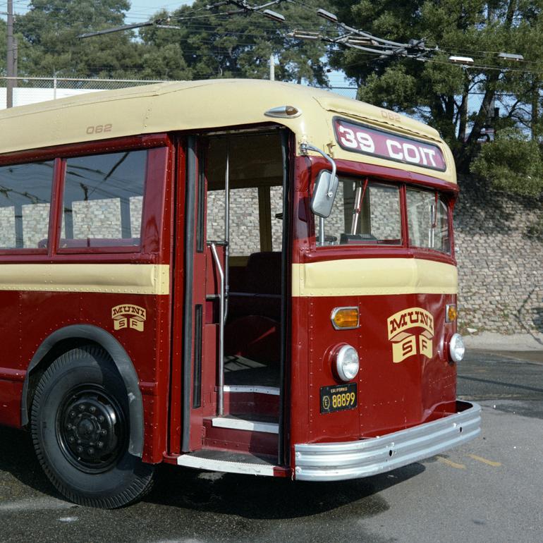 Vintage red and cream motor coach 062 with maroon and yellow paint scheme and Muni logo, parked on street.