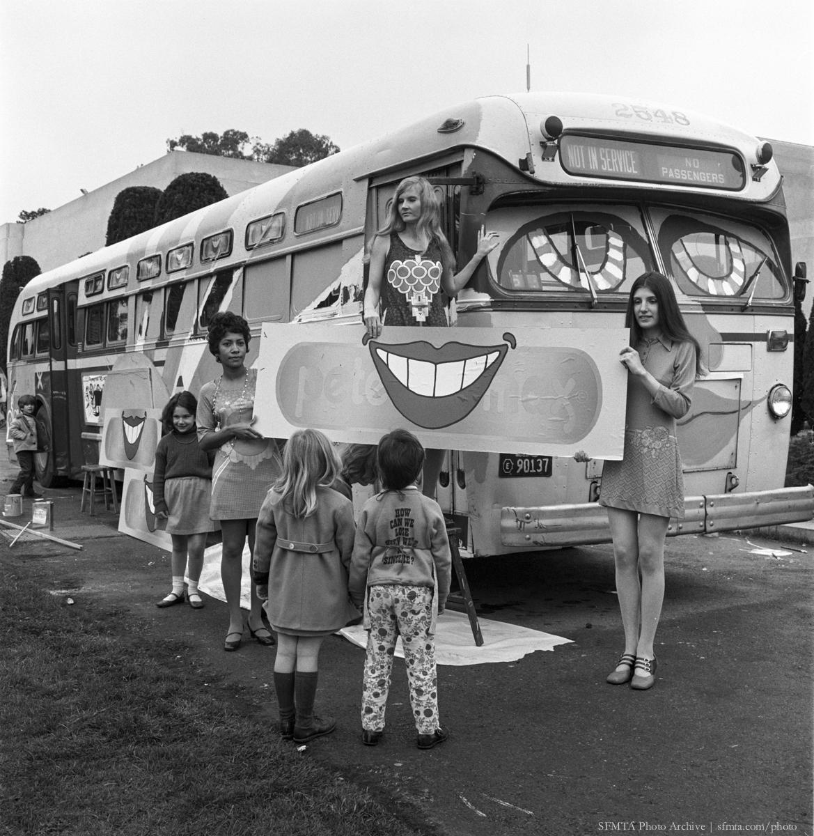 Children and adults paint a large smiling face on the side of a Mack bus for a Peter Max art exhibit, 1970.