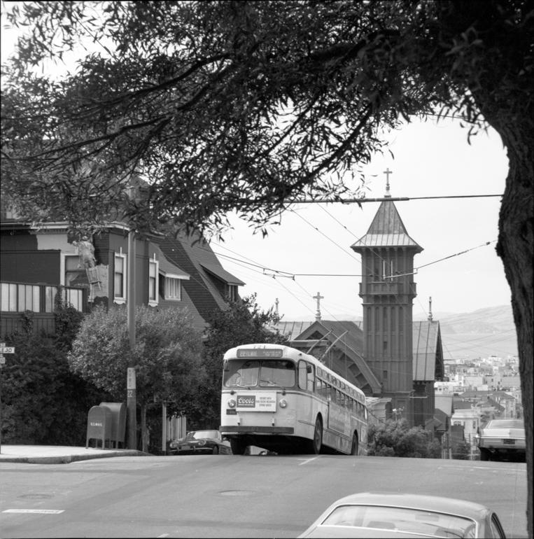 Trolley bus climbing steep hill on Steiner Street in Pacific Heights neighborhood with church tower visible in background.