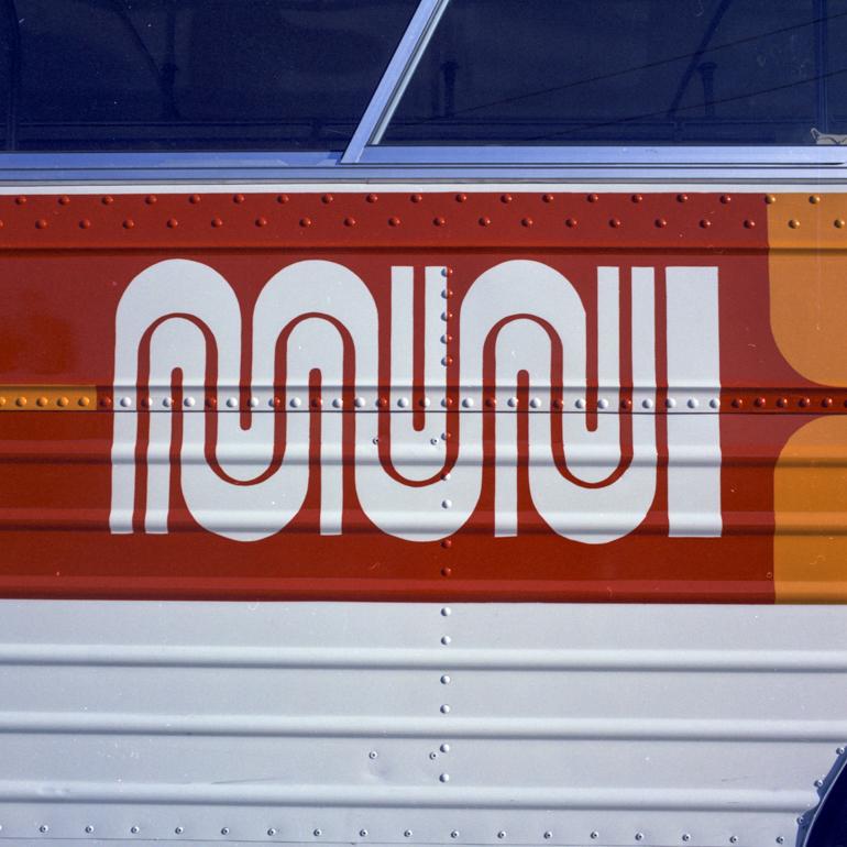 Red and white Muni transit bus panel with geometric logo design and riveted metal details.