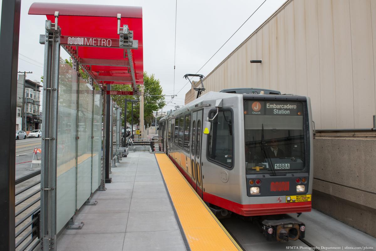 Light rail train at Balboa Park Station platform with red Metro shelter and yellow tactile warning strip.
