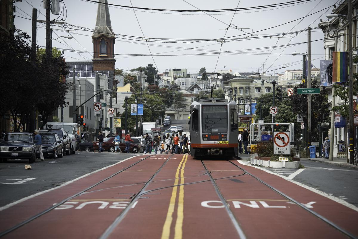 Light rail vehicle traveling south on Church Street in a red transit-only lane with pedestrians and buildings visible.