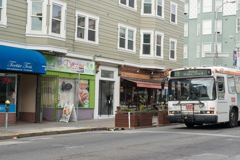 Southbound 19 Polk Muni bus stopped at curb on Polk Street with storefronts and residential buildings.