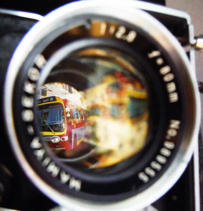 Red and yellow vintage bus reflected in camera lens