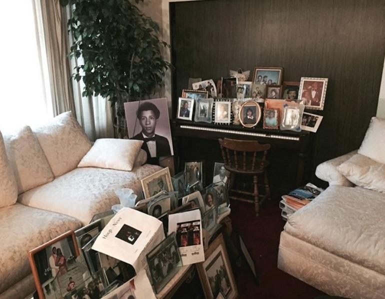 Living room with cream-colored furniture, dark accent wall, piano with framed family photos, and additional photos displayed on coffee table.