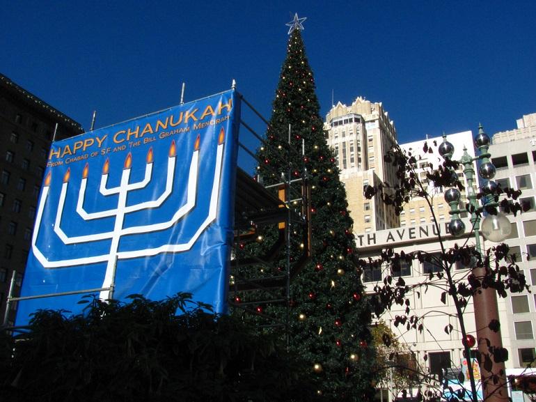 Menorah and Christmas tree displayed in Union Square during holiday season with city buildings in background.