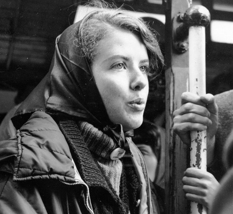 Woman in headscarf and quilted jacket holding cable car pole, black and white photograph.