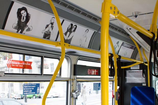 Interior of Muni bus displaying black and white artwork on upper panels above windows with yellow handrails visible.