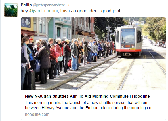 Large crowd of commuters waiting in line next to N-Judah light rail shuttle on San Francisco street.
