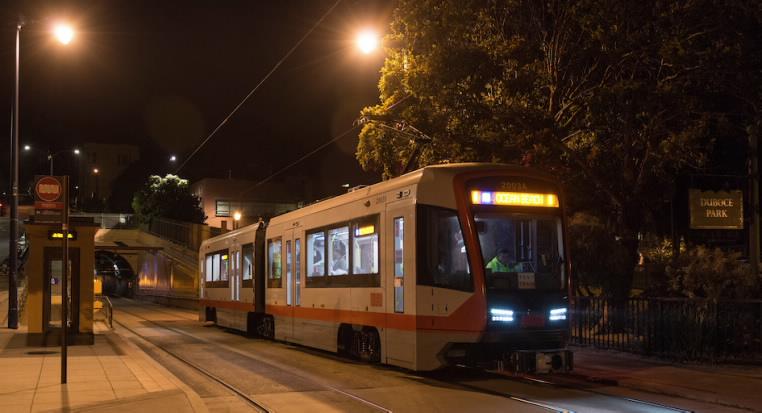 Light Rail Vehicle stopped at Duboce Park station at night with illuminated headlights and station lighting.