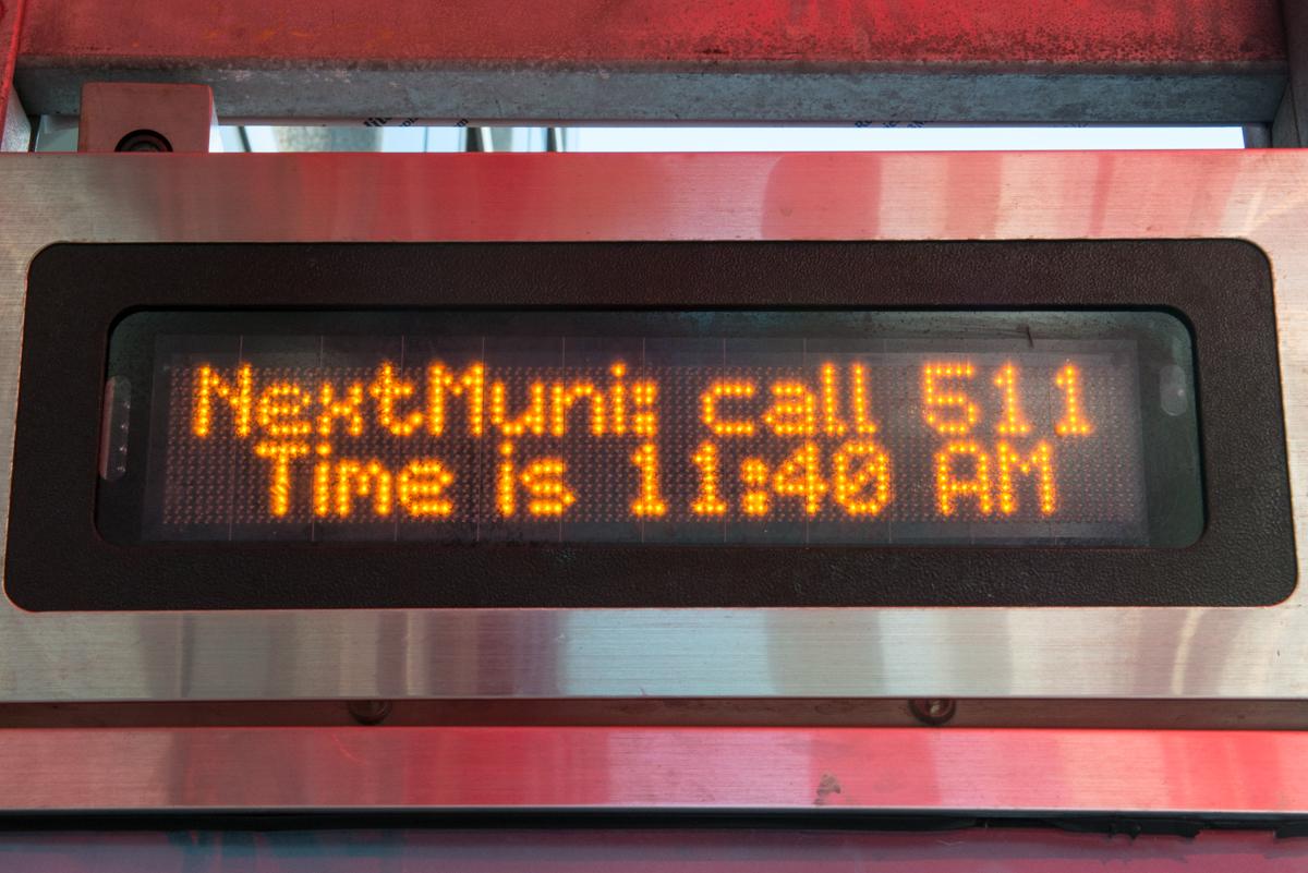 NextMuni shelter sign displaying "Next Muni call 511 Time is 11:48 AM" in orange text on black display.