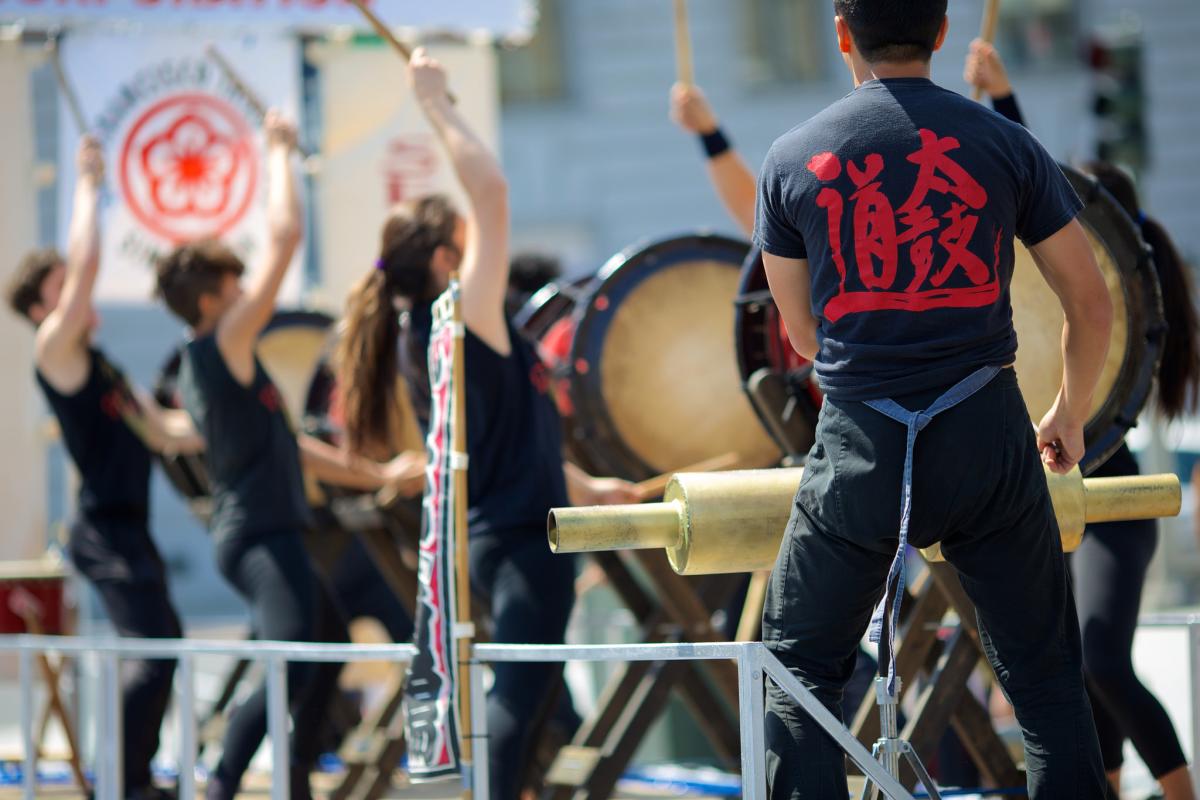Taiko drummers perform in black shirts with red lettering at the Cherry Blossom Festival.
