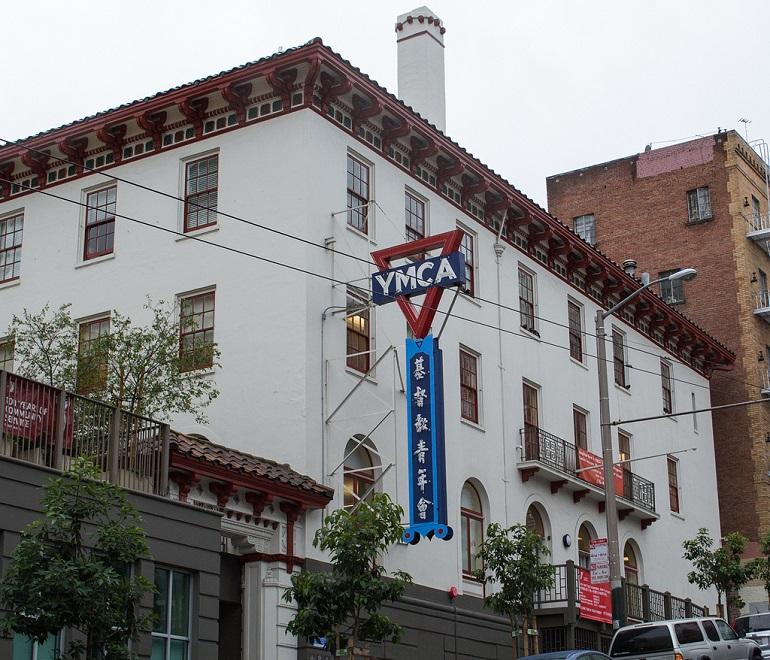 Chinatown YMCA building with red and white facade, blue vertical sign, and brick building adjacent on Sacramento Street.