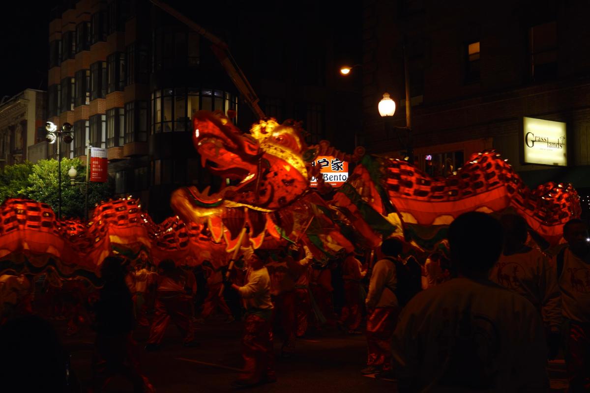 Red and gold illuminated Chinese dragon puppet carried by participants during nighttime parade on city street.