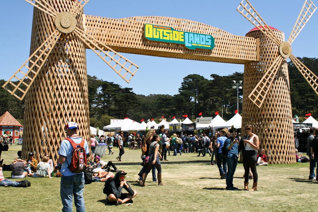 Large wooden windmill entrance gate at Outside Lands festival with crowds and white tents visible in sunny park setting.