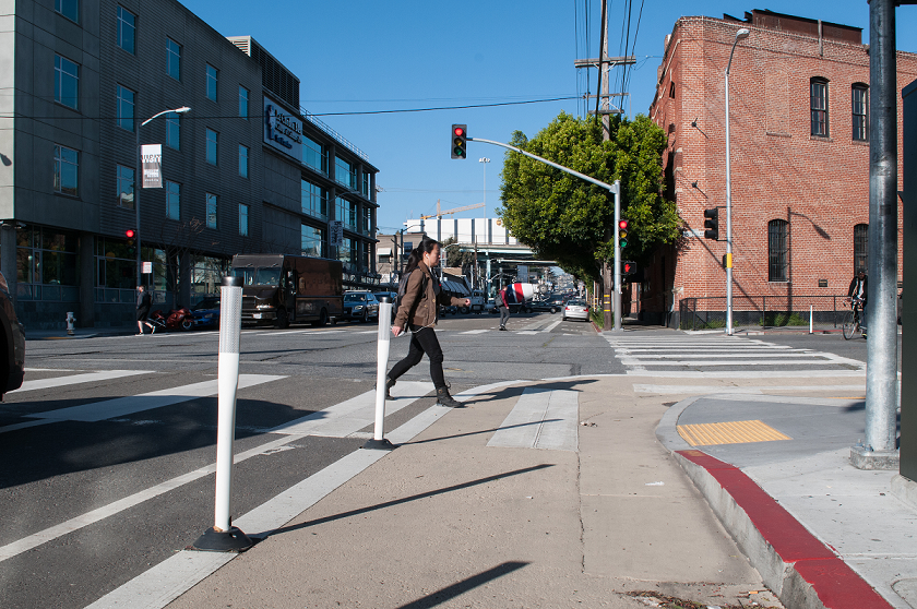 Pedestrian safety zone marked with red and yellow paint at street corner intersection with traffic signal.