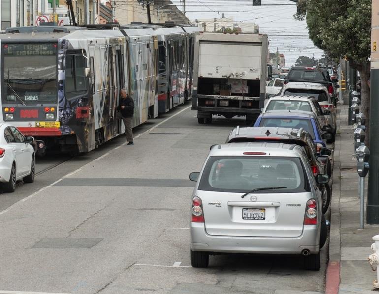 Parked cars line the curb as a Muni L Taraval train passes on Taraval Street.