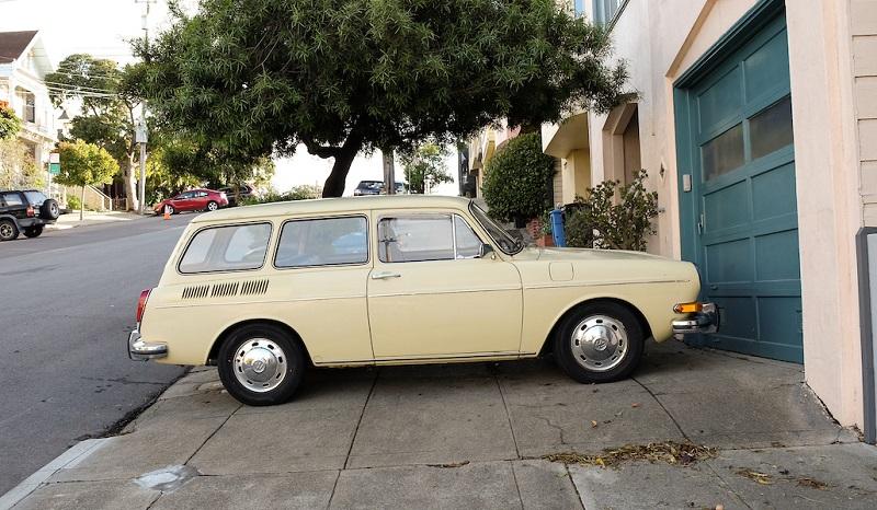 Cream-colored vintage Volkswagen parked on sidewalk in front of teal garage door.