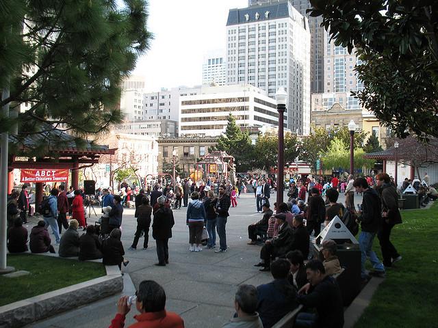 Crowd of people gathered in Portsmouth Square on a sunny afternoon with downtown buildings in background.