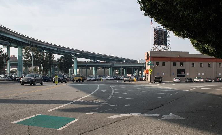 Intersection beneath elevated highway with traffic signals, street markings, and brick building with water tower.