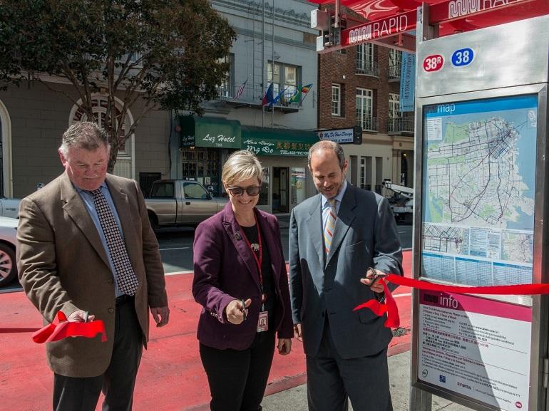 Three officials cut red ribbon at Muni bus shelter on Geary Street during Rapid transit project unveiling.