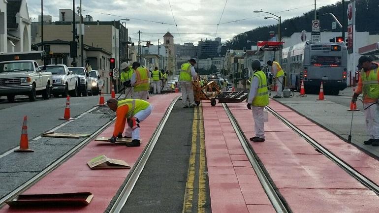 Workers in safety vests install red thermoplastic tiles around streetcar tracks on Judah Street.