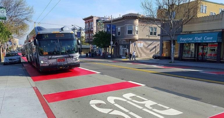 # Alt Text</p>
<p>14 Mission trolley bus on red transit lane on Mission Street with storefronts and buildings visible.