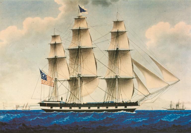 Three-masted sailing ship under full sail on blue ocean waters, American flag visible on hull.